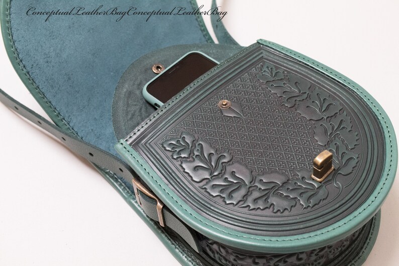 May include: A teal green leather satchel bag with a flap closure and a decorative floral design. The bag has a small pocket on the front that can fit a phone. The bag has a strap that can be adjusted to fit different body sizes.