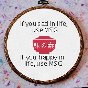 Może przedstawiać: Haft krzyżykowy w drewnianym tamborku. Biała tkanina zawiera tekst "If you sad in life, use MSG" i "If you happy in life, use MSG". Czerwona grafika miski z japońskim tekstem znajduje się na środku.