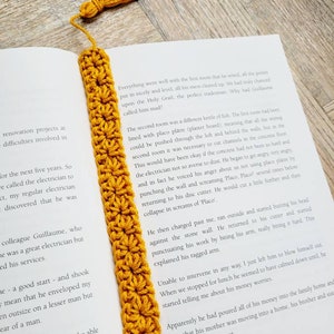 May include: A close-up of a yellow crocheted bookmark with a tassel. The bookmark is placed on a book with text about a renovation project and an electrician.