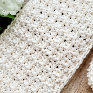 May include: Close-up of a crocheted fabric with a textured pattern in a cream color.