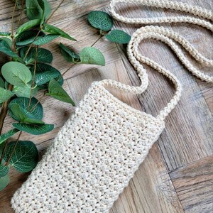 May include: A small, off-white crocheted crossbody bag with a long strap. The bag is made with a simple stitch pattern and has a rectangular shape.