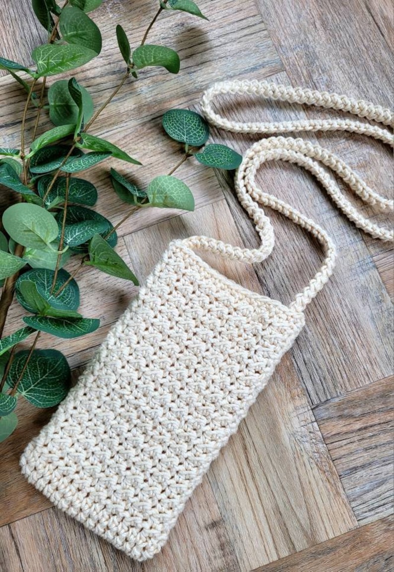 May include: A small, off-white crocheted crossbody bag with a long strap. The bag is made with a simple stitch pattern and has a rectangular shape.