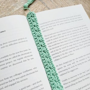 May include: A light green crocheted bookmark with a tassel. The bookmark is placed on a book with text about a renovation project.