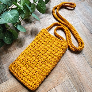 May include: A mustard yellow crocheted crossbody bag with a long strap. The bag is made of a thick yarn and has a simple, minimalist design.