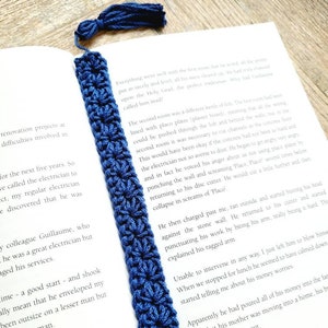 May include: A close-up of a blue crocheted bookmark with a tassel. The bookmark is lying on top of an open book with text about a renovation project.