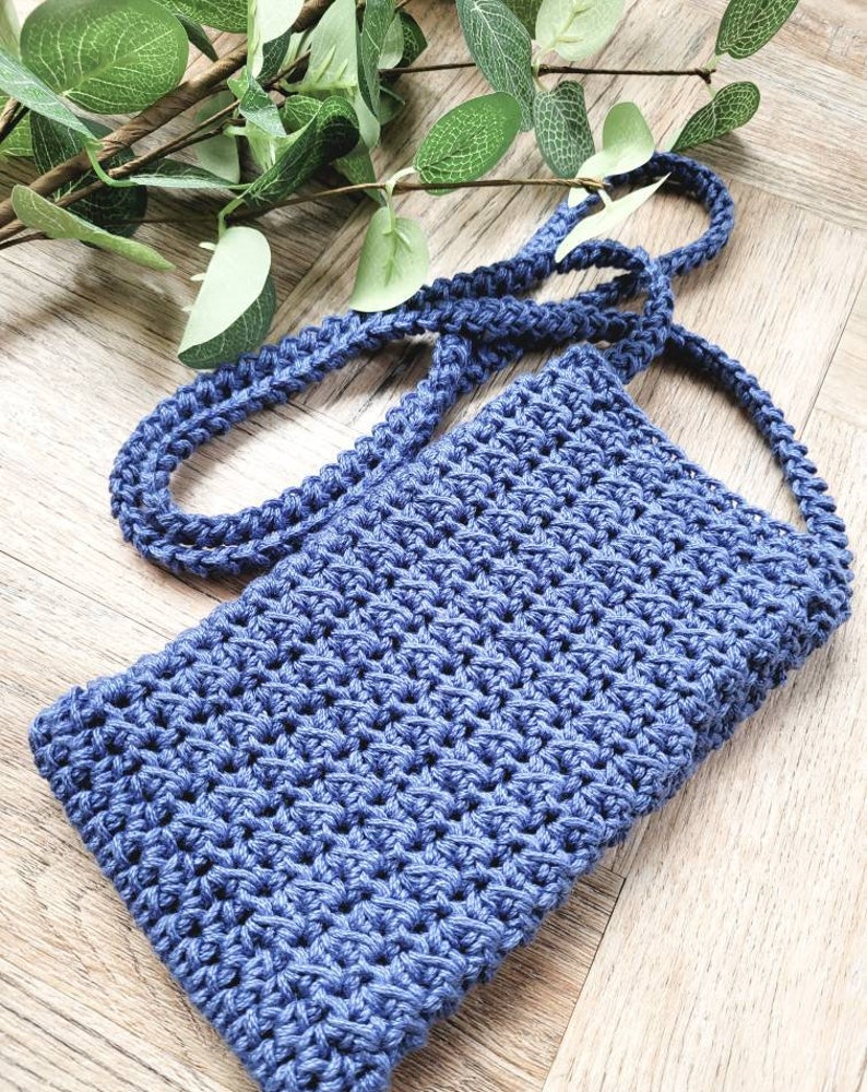 May include: A small blue crocheted bag with a long strap. The bag is made with a simple stitch pattern and has a slightly textured surface.