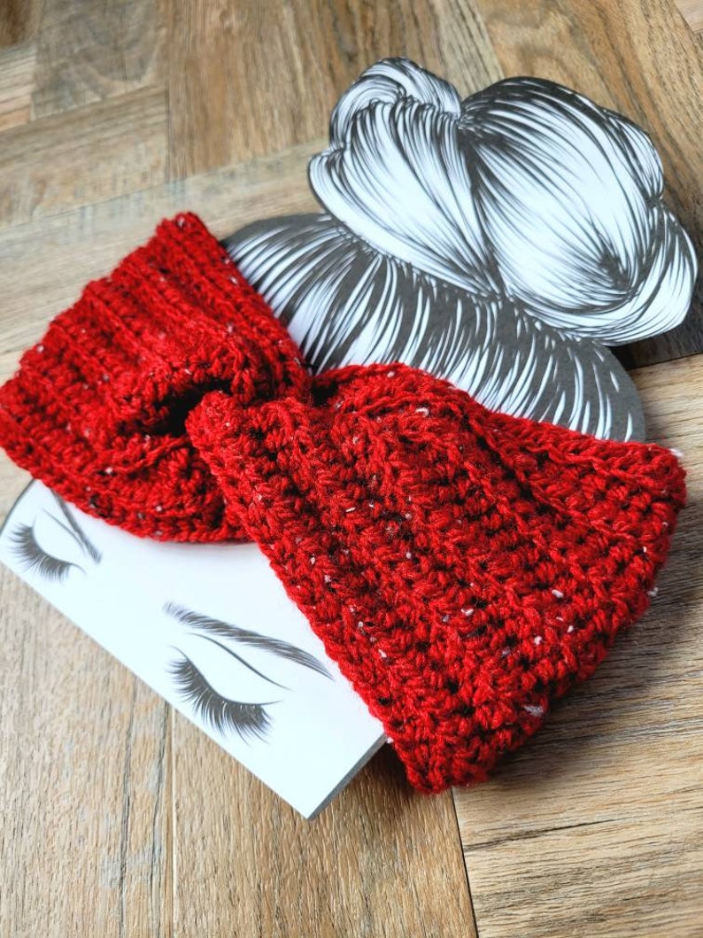 May include: Red crocheted headband with a knotted bow. The headband is made with a chunky yarn and has a speckled texture.