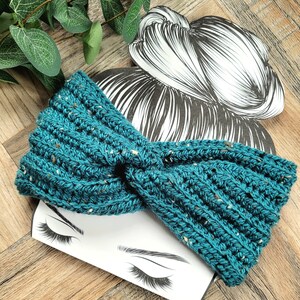 May include: A teal blue crocheted headband with a knotted design. The headband is on a white background with a drawing of a woman's face.