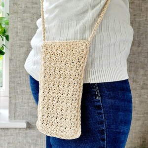 May include: A beige crocheted crossbody bag worn over a white shirt and blue jeans.