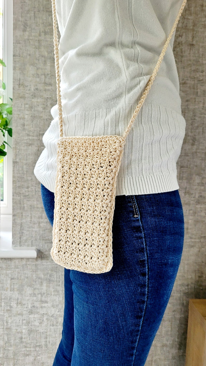 May include: A beige crocheted crossbody bag worn over a white shirt and blue jeans.