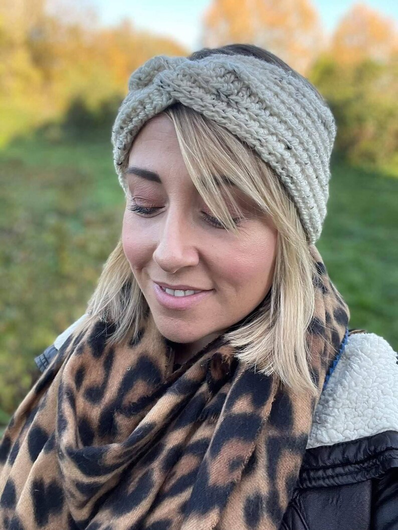May include: A woman wearing a beige crocheted headband with a knotted design. She is also wearing a leopard print scarf and a black jacket.