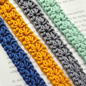 May include: Four crocheted bookmark straps in different colors: blue, yellow, gray, and green. Each strap is made with a star stitch pattern.