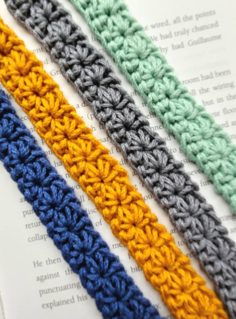 May include: Four crocheted bookmark straps in different colors: blue, yellow, gray, and green. Each strap is made with a star stitch pattern.