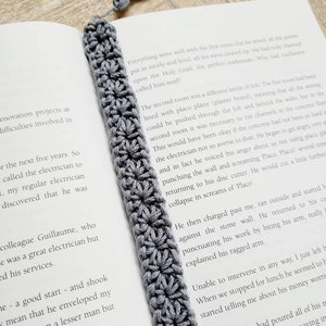 May include: A gray crocheted bookmark with a tassel. The bookmark is laying on top of an open book with text about a tradesman.