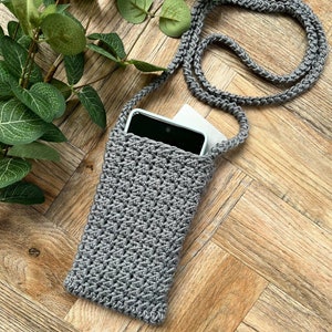 May include: A gray crocheted phone case with a long strap. The case is lying on a wooden surface with a smartphone inside.
