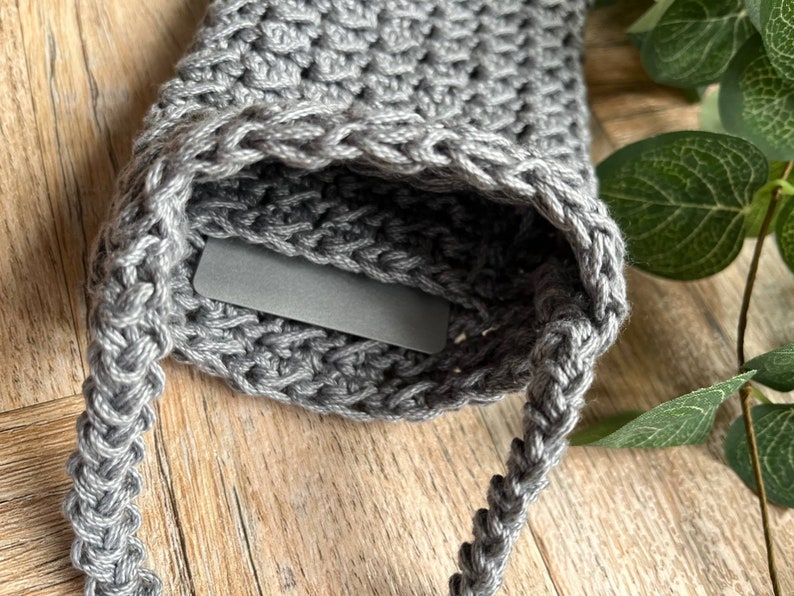 May include: Gray crocheted bag with a braided strap. The bag has a small pocket on the front.
