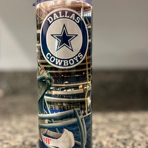 Puede incluir: Un vaso de acero inoxidable con el logotipo de los Dallas Cowboys y una imagen del estadio. El vaso tiene un diseño azul, blanco y rojo.