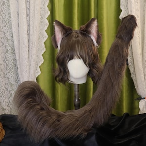 May include: A brown faux fur cat tail and matching ear headband set. The ears are brown with pink inner ears and white trim. The tail is long and fluffy. The set is displayed on a mannequin head with brown wavy hair.