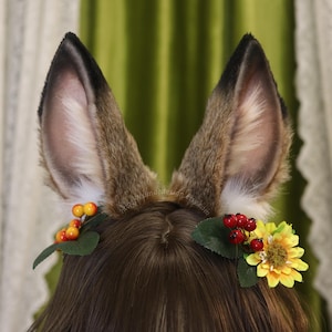 Può includere: Una fascia per capelli con orecchie di cervo in finta pelliccia marrone e nera. Le orecchie sono decorate con una piccola composizione floreale di bacche rosse e un fiore giallo. Accessorio in costume.