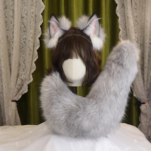 May include: A gray faux fur tail and matching headband with wolf ears. The ears are white with gray and pink accents. The tail is long and fluffy, and the set is displayed on a mannequin head.