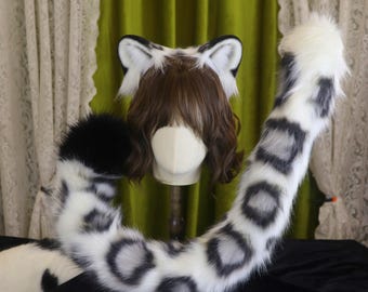 Puede incluir: Un conjunto de cosplay de piel sintética con temática de leopardo de las nieves. Incluye una diadema con orejas negras y blancas y una cola larga. La cola y las orejas son blancas con manchas negras.