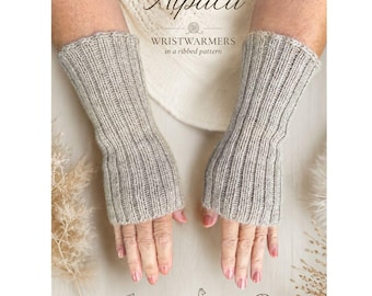 Op de afbeelding: Een paar lichtgrijze, geribbelde gebreide polswarmers van alpacavezels. De tekst op de afbeelding luidt PURE Alpaca WRISTWARMERS in a ribbed pattern, Soft & Natural, 100% Alpaca en Handmade with Care, vergezeld door iconen van een blad, een alpaca en een bol wol.