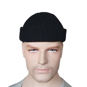 K&ouml;nnte beinhalten: Eine schwarze Strickm&uuml;tze mit umgeschlagenem Rand. Die M&uuml;tze wird auf einem Schaufensterkopf pr&auml;sentiert. Diese klassische M&uuml;tzenform ist f&uuml;r kaltes Wetter geeignet.