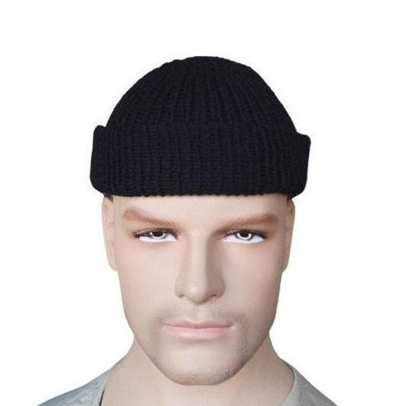 K&ouml;nnte beinhalten: Eine schwarze Strickm&uuml;tze mit umgeschlagenem Rand. Die M&uuml;tze wird auf einem Schaufensterkopf pr&auml;sentiert. Diese klassische M&uuml;tzenform ist f&uuml;r kaltes Wetter geeignet.