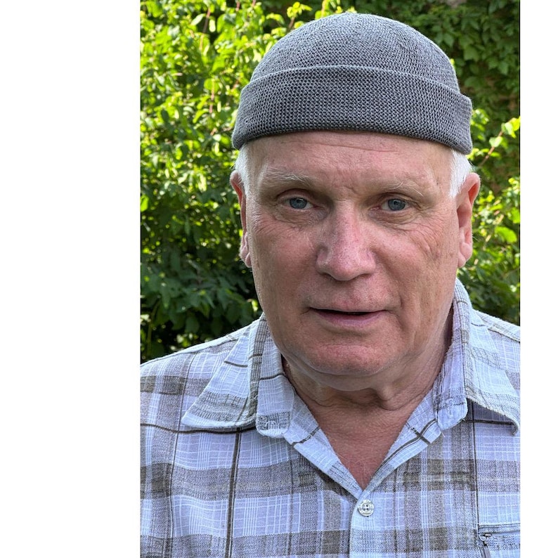 May include: A grey knit beanie with a rolled cuff edge. The beanie features a textured, woven fabric construction with a rounded crown. The material has a consistent grey tone throughout, providing a simple and functional head covering design.