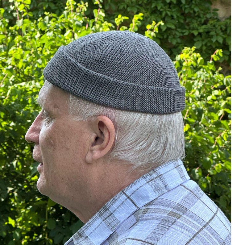 May include: A charcoal gray docker cap featuring a textured, knit construction with a thick, folded brim. The hat has a rounded crown and a snug fit, showcasing a consistent, fine-gauge weave pattern throughout the entire surface of the headwear.