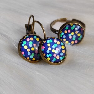 May include: A jewelry set featuring a pair of leverback earrings and a ring. The earrings and ring have a dark blue background with a pattern of colorful polka dots in yellow, pink, green, and orange. The metal has a bronze finish.