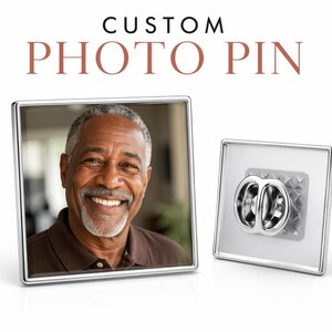 May include: Square photo pin with a silver border. The pin features a smiling man in a brown shirt. The text "CUSTOM PHOTO PIN" is displayed above the pin. The back of the pin has a silver clasp.
