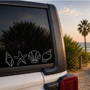 May include: White outline decals of a seashell, starfish, scallop shell, and conch shell are displayed on a vehicle window. The background shows a beach scene with palm trees, sand, and ocean waves, suggesting a coastal theme.