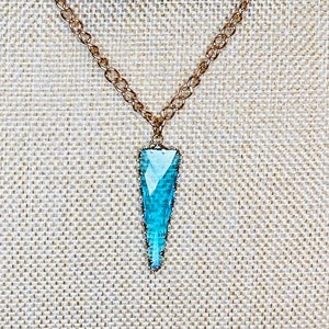 May include: A gold chain necklace with a turquoise blue crystal pendant shaped like a point.
