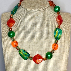 May include: A necklace made of green, orange, and red beads. The beads are various shapes and sizes, including round, square, and rectangular.