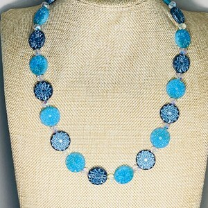 May include: A blue and white necklace with round, patterned beads. The beads are arranged in a gradient from dark blue to light blue.