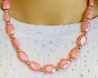 May include: A pink beaded necklace featuring large, faceted beads interspersed with small silver-colored beads. The necklace is displayed on a mannequin, showcasing the jewelry's design and color. The beads have a pearlescent sheen.