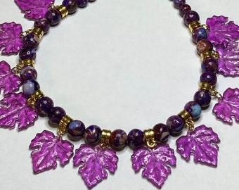 May include: A purple and gold necklace with a beaded chain and dangling purple leaf charms.