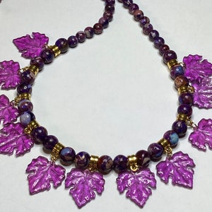 May include: A purple and gold necklace with a beaded chain and dangling purple leaf charms.