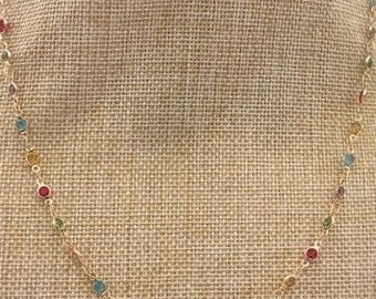 May include: A gold chain necklace with small, colorful round stones. The stones are red, green, and blue.