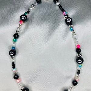 May include: A beaded necklace with black 8-ball beads, small black, white, silver, and iridescent beads. The necklace has a silver clasp and includes pink, blue, and green accents.