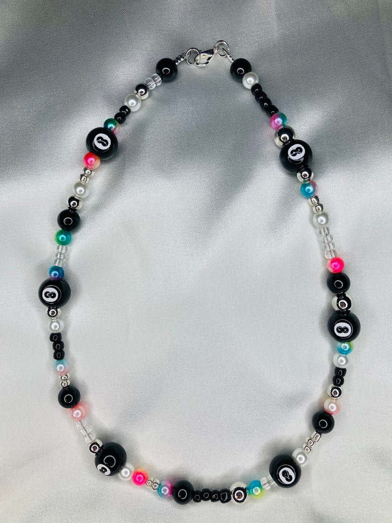 May include: A beaded necklace with black 8-ball beads, small black, white, silver, and iridescent beads. The necklace has a silver clasp and includes pink, blue, and green accents.