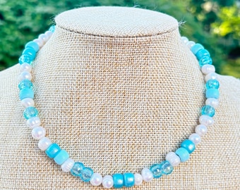 May include: A white and blue beaded necklace with a graduated colour scheme. The necklace is made with white pearls and light blue and dark blue glass beads.