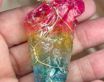 May include: A rainbow-colored crystal pendant wrapped in gold wire. The crystal is a deep red at the top, fading to yellow, then green, and finally blue at the bottom.