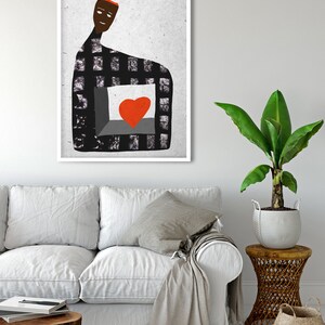 May include: Abstract art print featuring a figure with a checkered pattern and a red heart. The artwork has a white frame and is displayed in a living room setting with a white sofa, wooden table, and a potted plant.