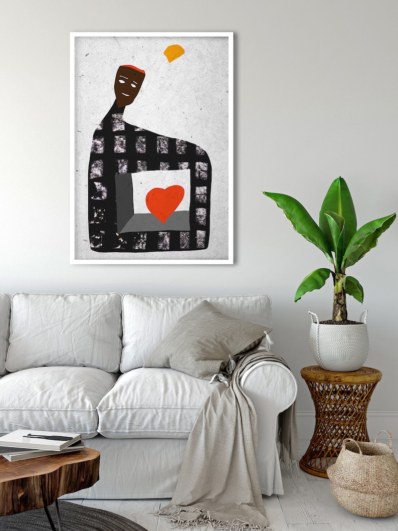 May include: Abstract art print featuring a figure with a checkered pattern and a red heart. The artwork has a white frame and is displayed in a living room setting with a white sofa, wooden table, and a potted plant.