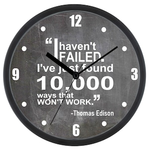Puede incluir: Reloj blanco y negro con fondo gris. La esfera del reloj tiene una cita de Thomas Edison: "No he FALLADO. Solo he encontrado 10.000 maneras que NO FUNCIONAN."