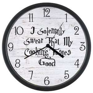 May include: A black framed clock with white woodgrain background. The clock face has black numbers and hands. The text on the clock face reads "I Solemnly Swear That My Cooking Tastes Good".