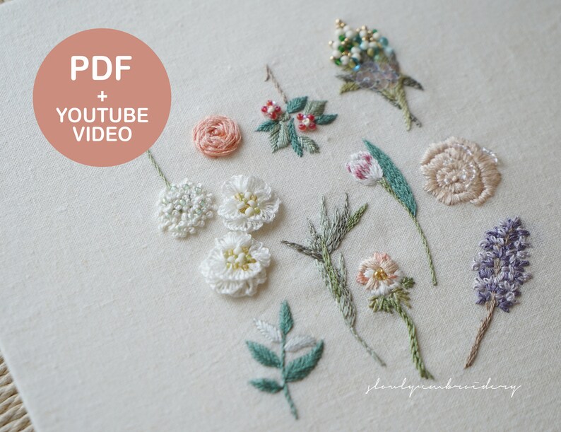以下が含まれることがあります： オフホワイトの生地の正方形に、パステルカラーの手刺繍の花柄がいくつかあります。刺繍には、詳細な花、葉、茎が含まれており、一部のデザインにはビーズが組み込まれています。「PDF + YOUTUBE VIDEO」というテキストがピンク色の円の中にあります。