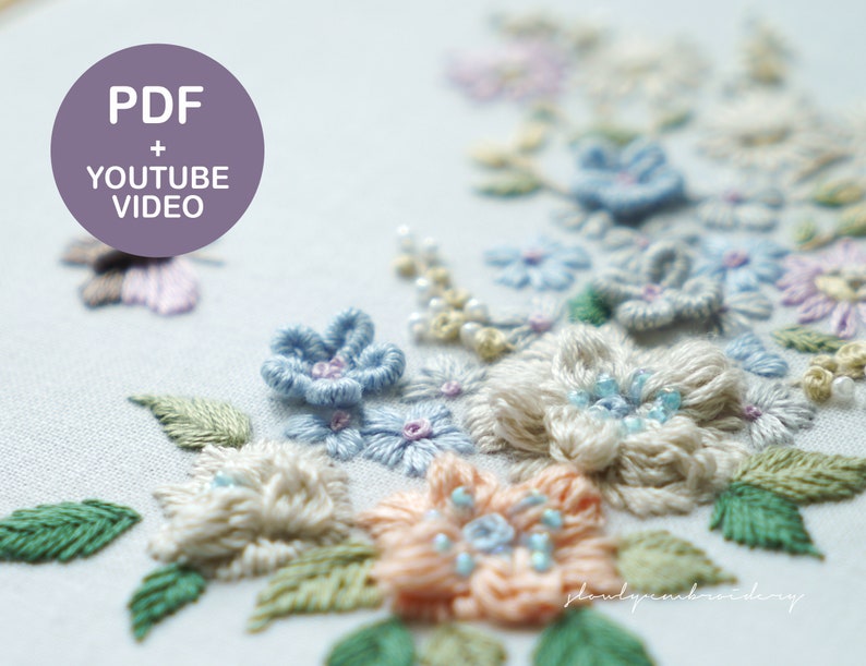 May include: Close-up of a floral embroidery design featuring pastel-colored flowers and green leaves. The flowers are in shades of blue, peach, and cream, with delicate bead accents. The text "PDF + YOUTUBE VIDEO" is in a purple circle.